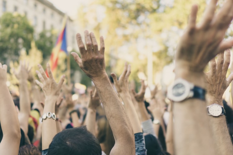Das Bild zeigt eine demonstrierende Menschenmenge, die ihre Hände in die Luft heben. 