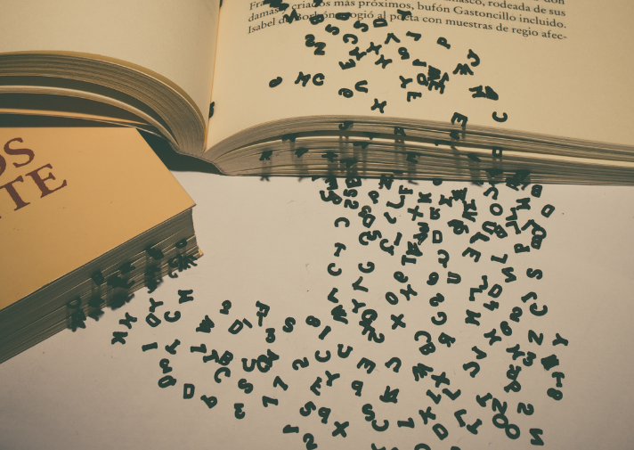 Ein offenes und ein geschlossenes Buch liegen schräg aufeinander, aus deren Seiten fallen einzelne Buchstaben heraus und sammeln sich daneben unsortiert. 