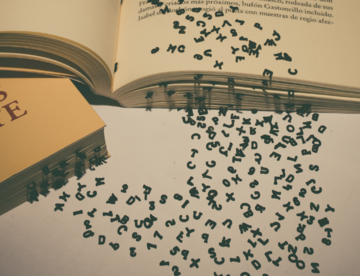 Ein offenes und ein geschlossenes Buch liegen schräg aufeinander, aus deren Seiten fallen einzelne Buchstaben heraus und sammeln sich daneben unsortiert. 
